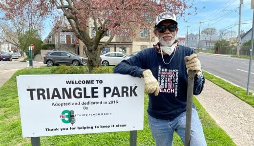 Man holding a shovel standing next to a sign that reads "Triangle Park"