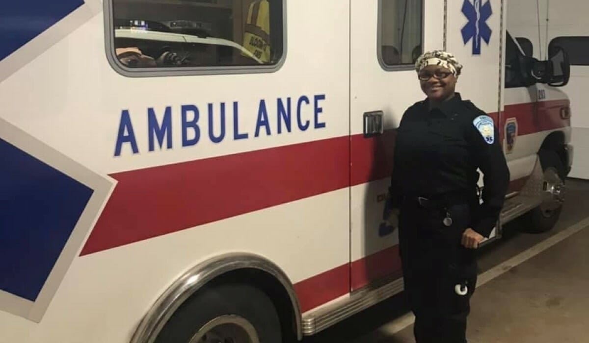 Woman in an EMT uniform stands next to an ambulance