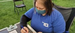 Woman seated at an outdoor table filling out medical patient cards.