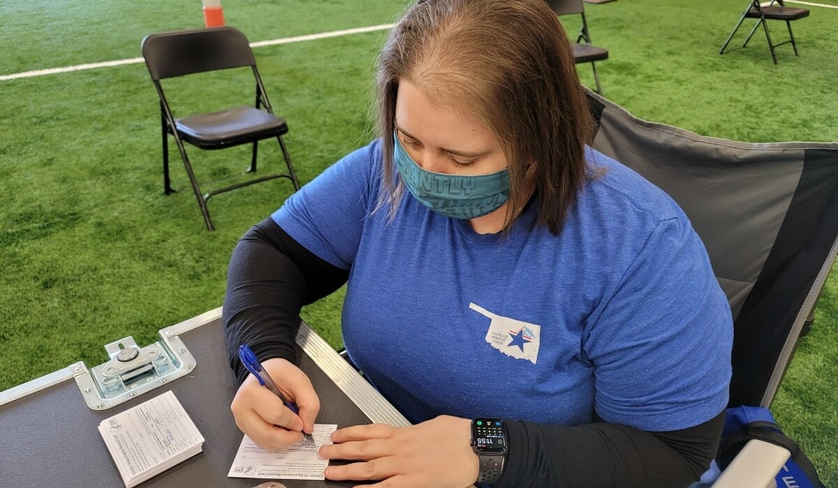 Woman seated at an outdoor table filling out medical patient cards.