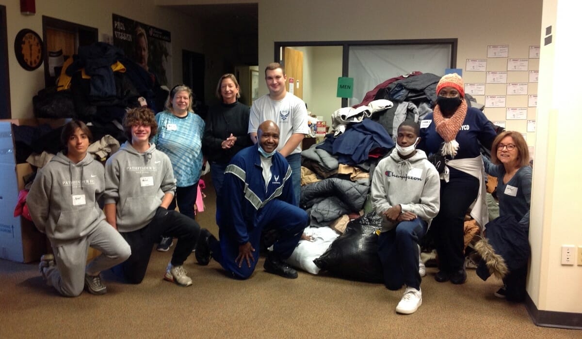 Group of people posing with a pile of donated winter coats.