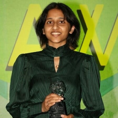 Girl in formal dress smiling and holding an award trophy.