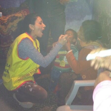 Woman in a reflective vest crouches to examine a child patient.