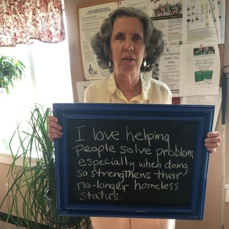 Woman holding a sign that says "I love helping people solve problems, especially when doing so strengthens their no-longer homeless status."