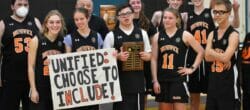 Group picture of a youth basketball team in orange and black uniforms. One player holds a sign reading "Unified: Choose to Include!"