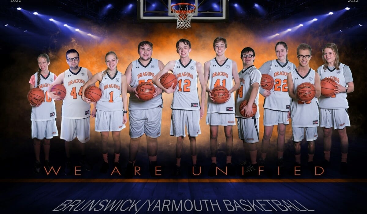 Group photo of a youth basketball team holding basketballs in white and orange uniforms.