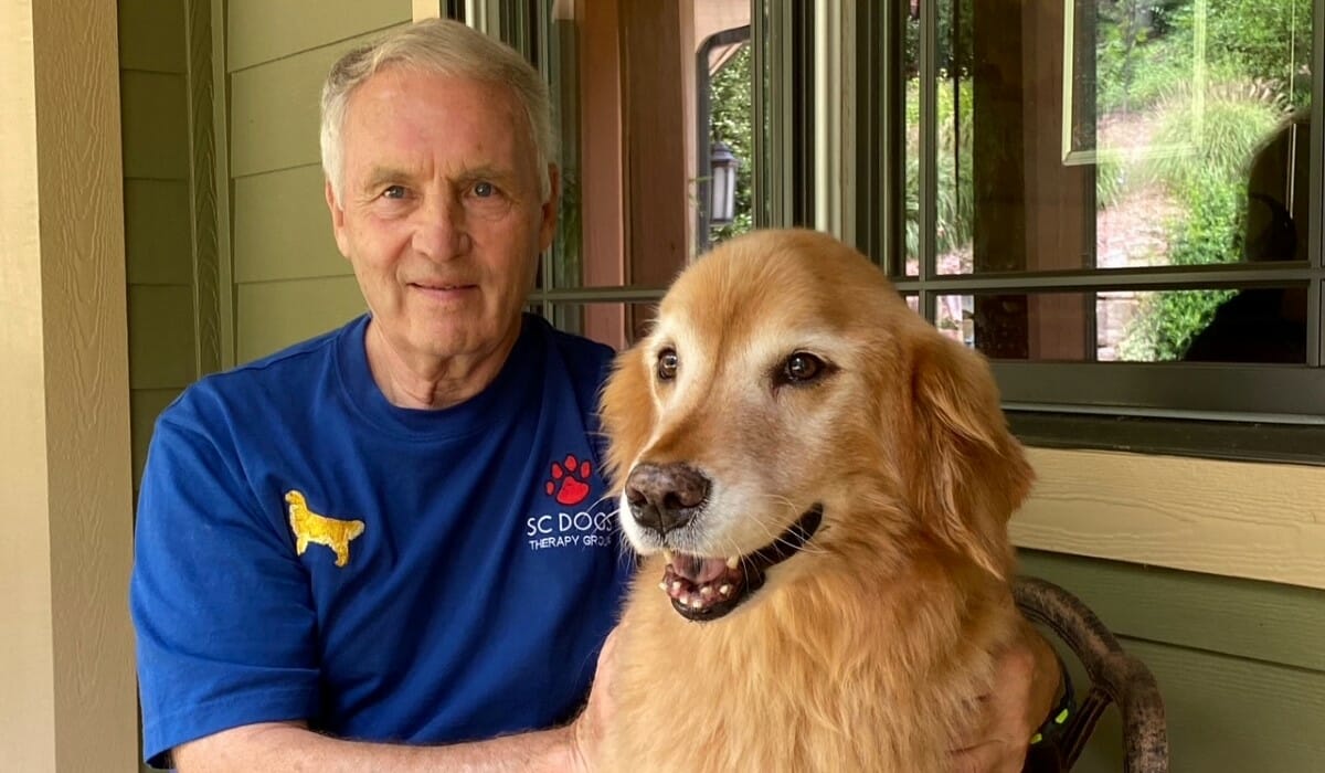 Man in a blue shirt poses with golden retriever.
