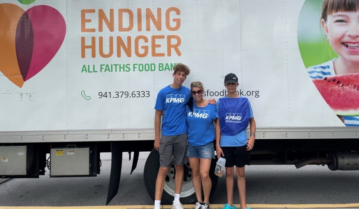 Three people wearing matching blue shirts emblazoned with the letters "KPMG" pose in front of a truck.