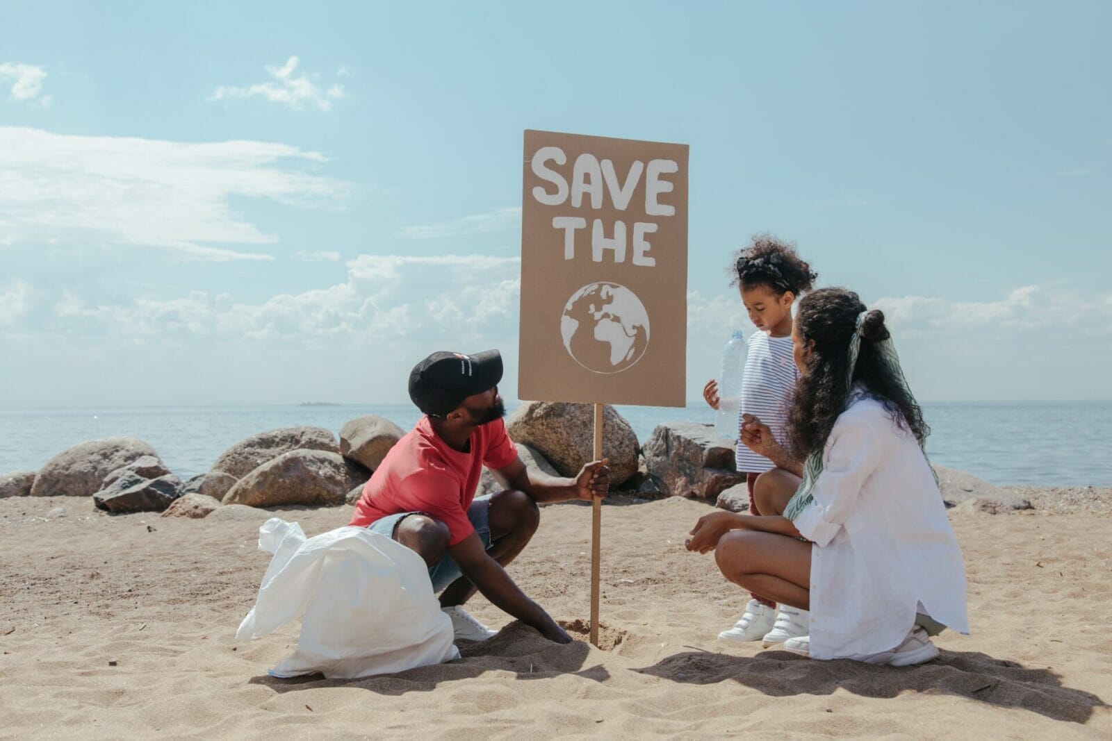 Family doing a beach clean up together with a sign that reads, "Save the Earth"