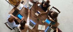 Aerial view of people sitting at a conference table with laptops. Two people are shaking hands across the table.