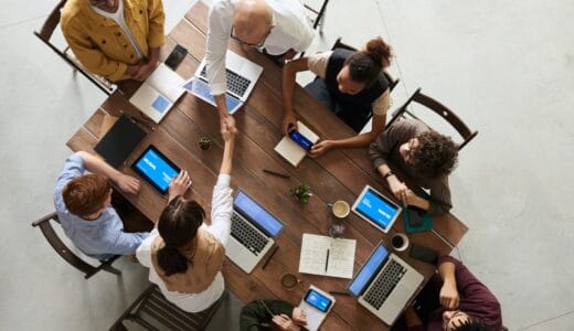 Aerial view of people sitting at a conference table with laptops. Two people are shaking hands across the table.